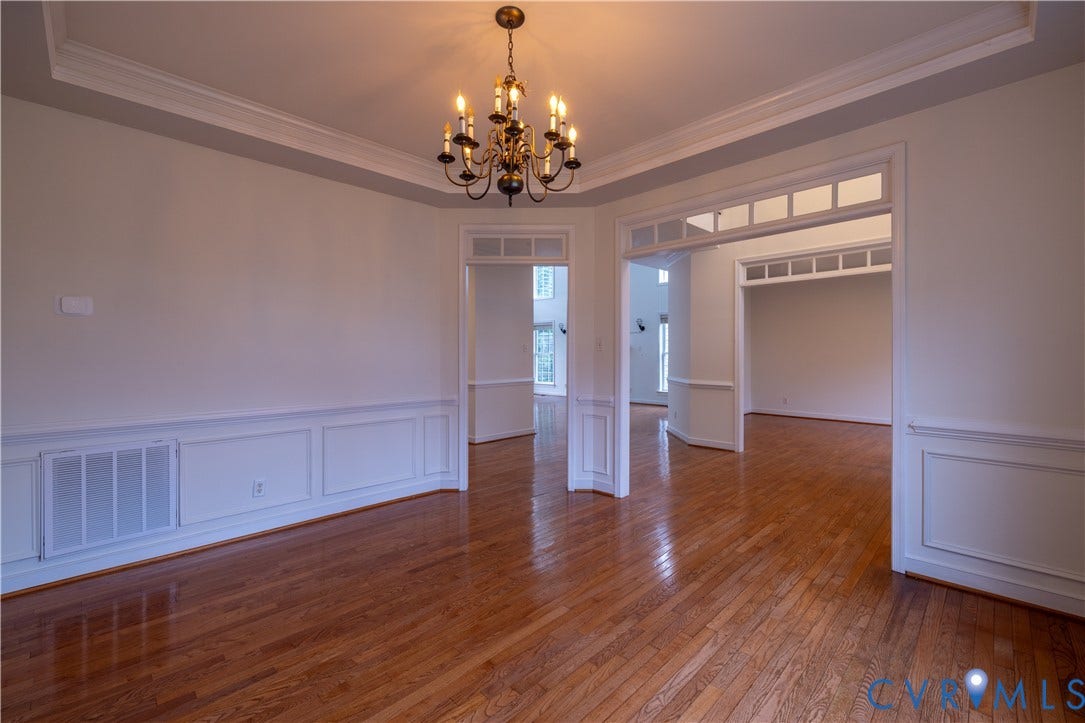 Hardwood flooring, tray ceiling, chandelier lighting, wainscoting, and cased openings with transom windows