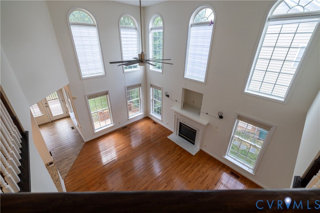 Soaring ceilings with multiple arched windows, rich wood-finish flooring, and a fireplace with a white mantel and surround