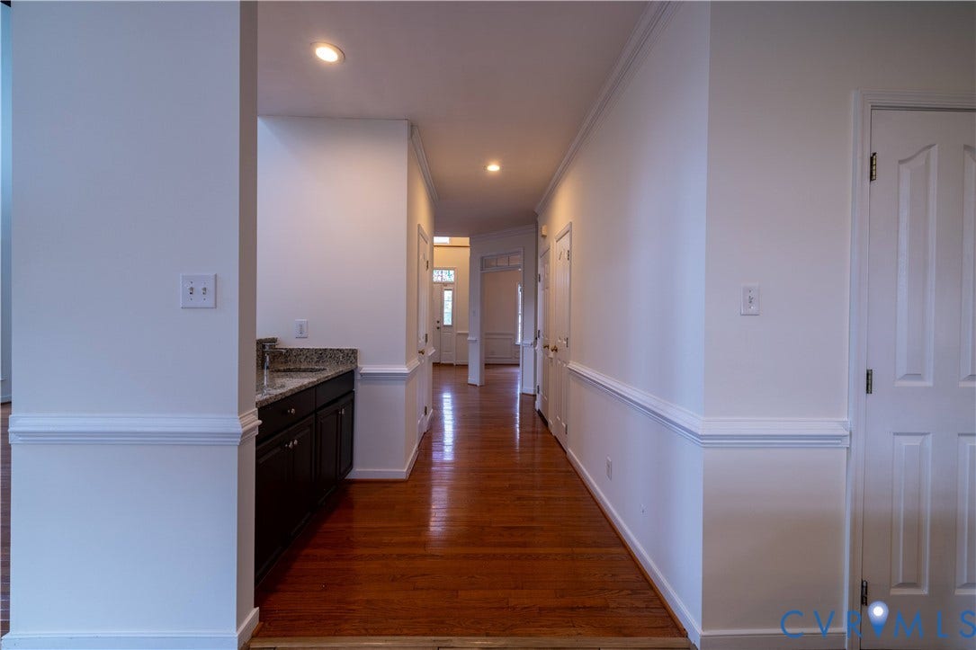 Wood-finish flooring throughout, recessed lighting, white panel doors, built-in cabinetry with stone countertop, and wainscoting