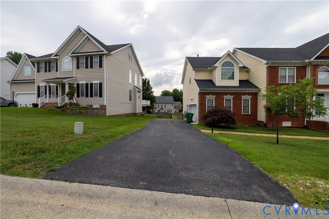 Paved driveway leading to a residence with a two-car garage, featuring a covered entry porch and multiple arched windows