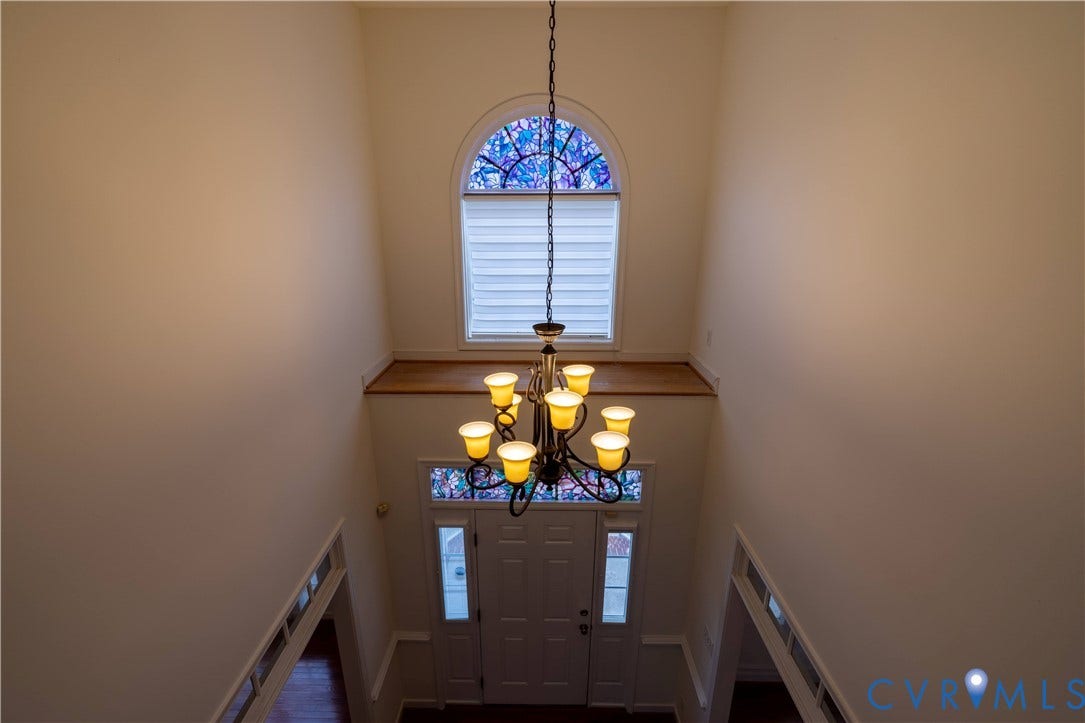 Foyer featuring a chandelier, vaulted ceiling, stained glass arched window, and a white paneled entry door with sidelights