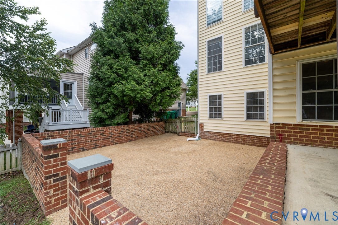 Defined outdoor space featuring brick half walls with stone caps, a gravel surface, and a wooden fence with a gate