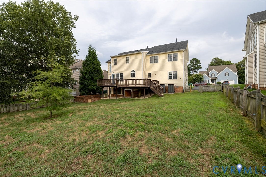 Expansive backyard featuring a wood deck, wood privacy fencing, mature trees, and a brick planter