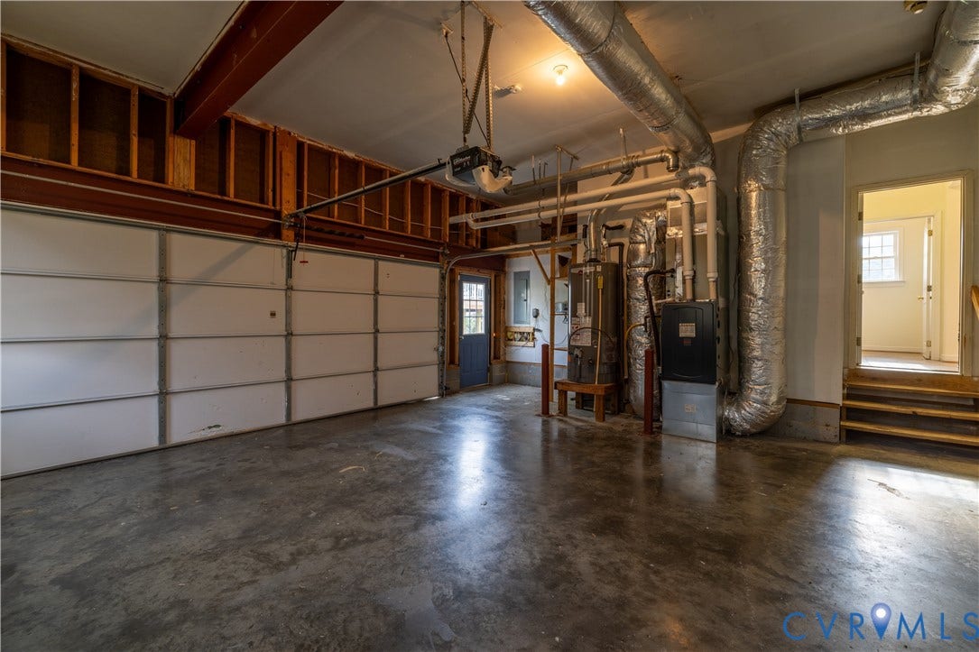 Spacious garage featuring a concrete floor, exposed wood framing, and white panel garage door