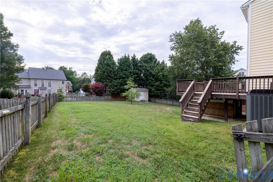 Expansive fenced backyard featuring a wood deck with stairs, a storage shed, and mature perimeter trees