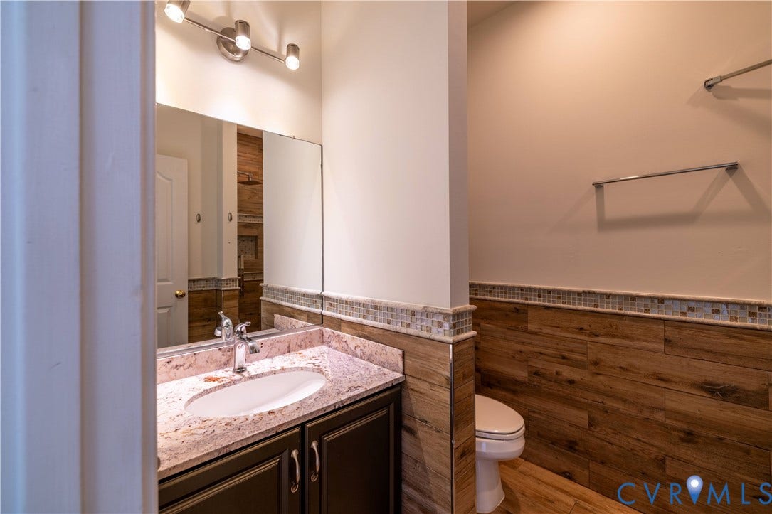 Vanity with an undermount sink, granite countertop, wood-finish wall paneling, mosaic tile accent, and a coordinating wood-finish floor