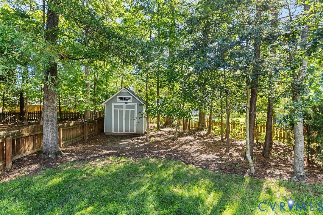Manicured lawn with a detached storage shed, framed by mature trees and a wood fence