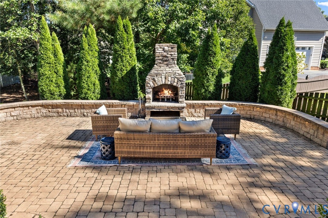 Expansive paver patio featuring a stone fireplace, retaining wall, and mature privacy landscaping
