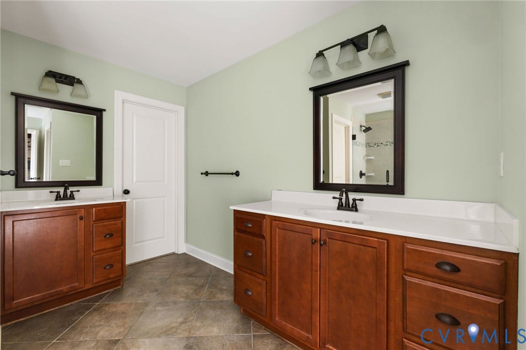 Dual vanity with wood-finish cabinetry, white countertops, tile flooring, and individual framed mirrors with integrated lighting
