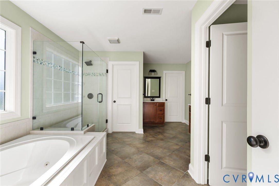 Spacious bathroom featuring a glass-enclosed shower with tile surround, a built-in soaking tub, and a single window for natural light