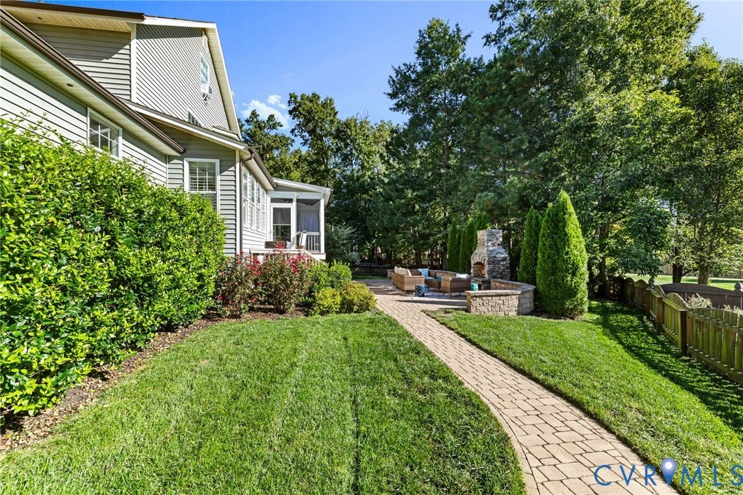 Manicured lawn, paver pathway, stone fireplace, screened porch, and mature landscaping