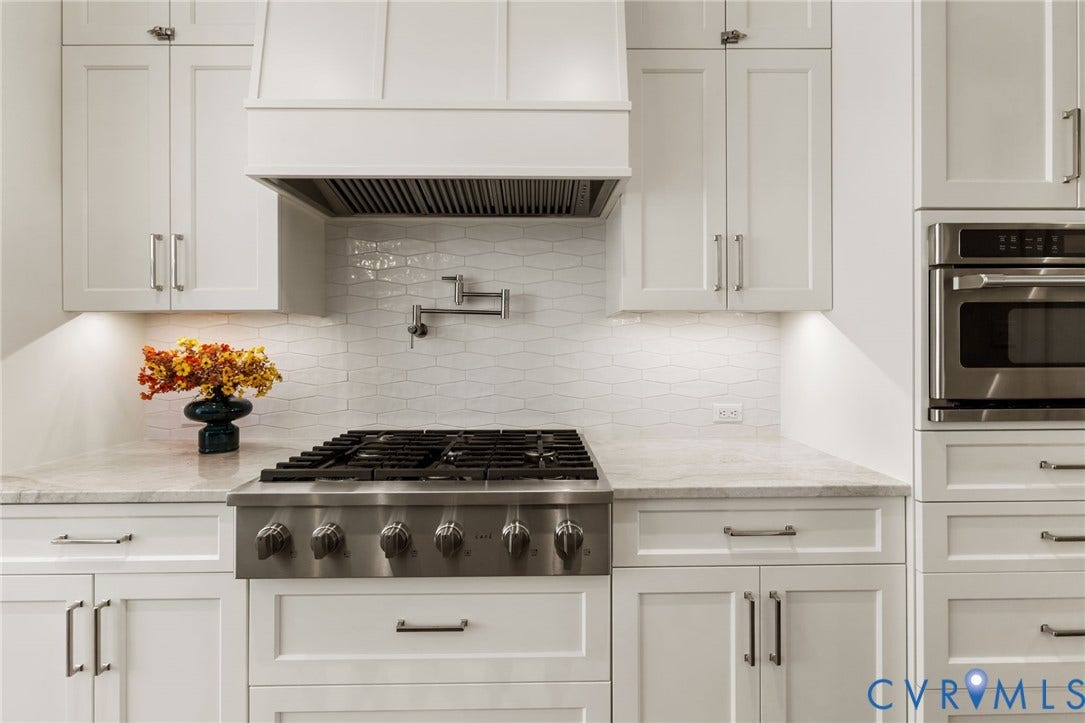 White shaker cabinetry, stainless steel range, white wave-patterned tile backsplash, wall-mounted pot filler, built-in stainless steel oven