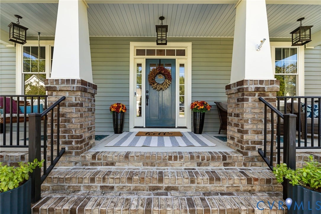 Brick and concrete front porch with steps, featuring two substantial white pillars and black metal railings