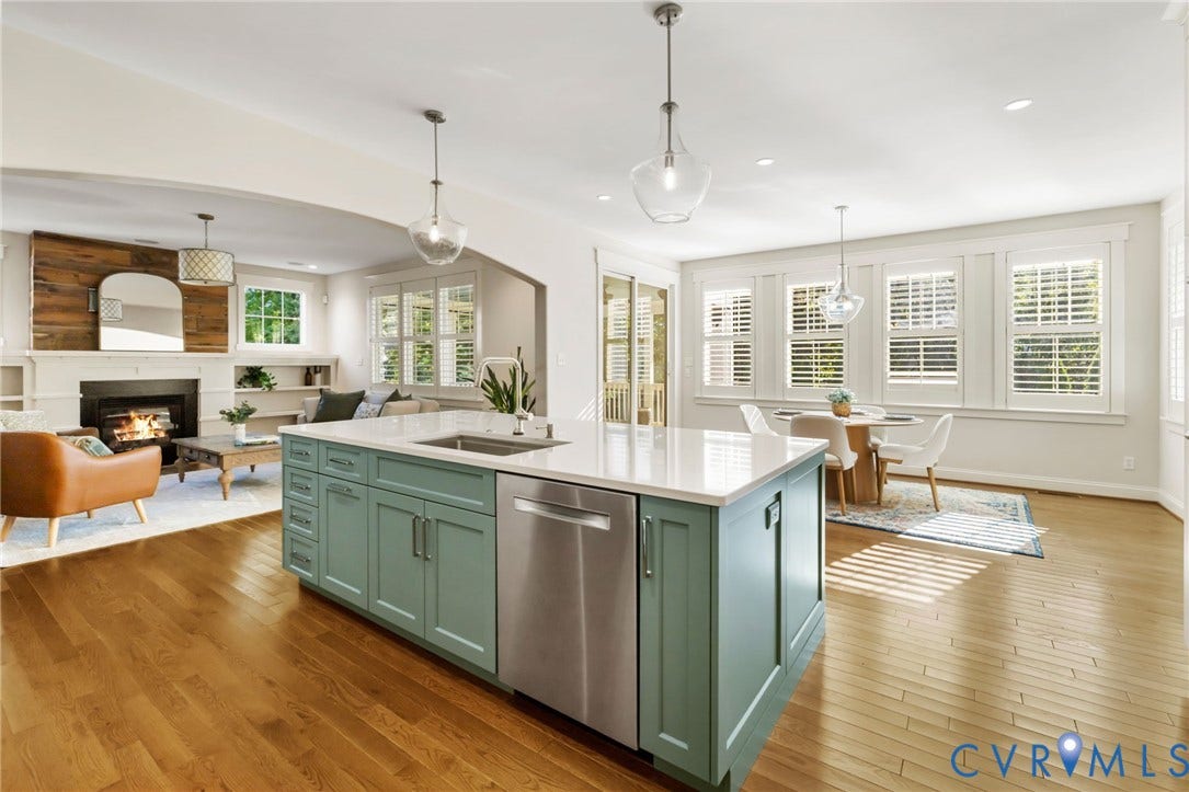 Light wood-finish flooring throughout, complemented by a kitchen island with light green cabinetry and integrated stainless steel appliances