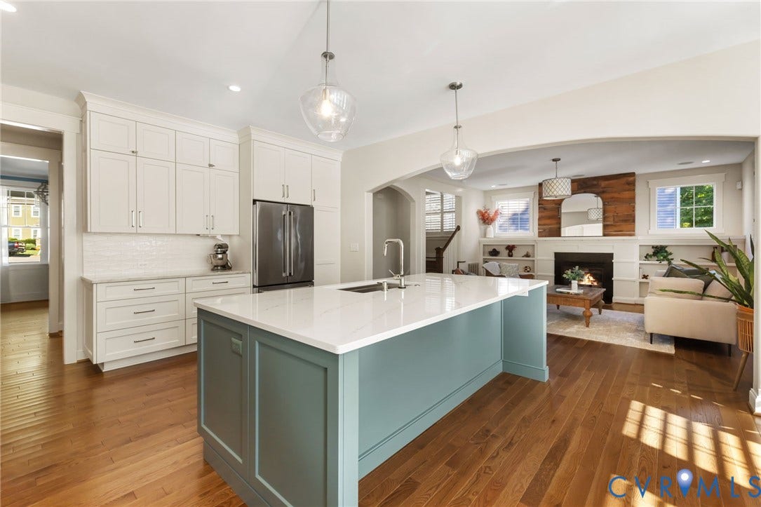 Hardwood-finish flooring, a kitchen island with a light-toned countertop, white cabinetry, and stainless steel appliances