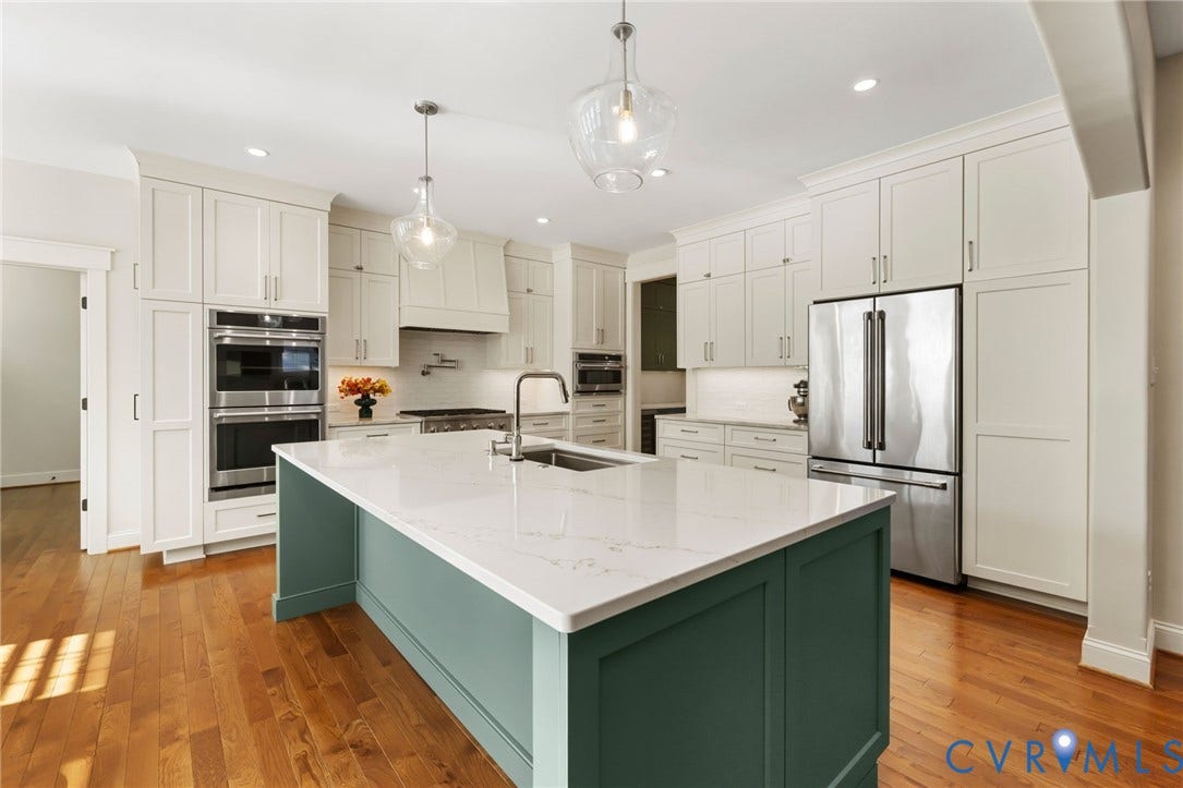 Kitchen featuring a large central island with a white countertop, stainless steel appliances, custom cabinetry, and wood-finish flooring