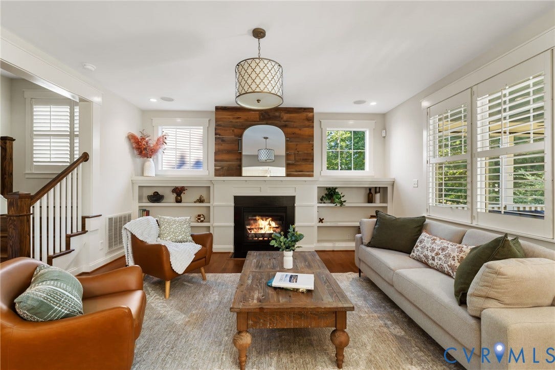 Hardwood flooring, fireplace with a wood-paneled accent wall, built-in shelving, white plantation shutters, and a decorative ceiling light fixture