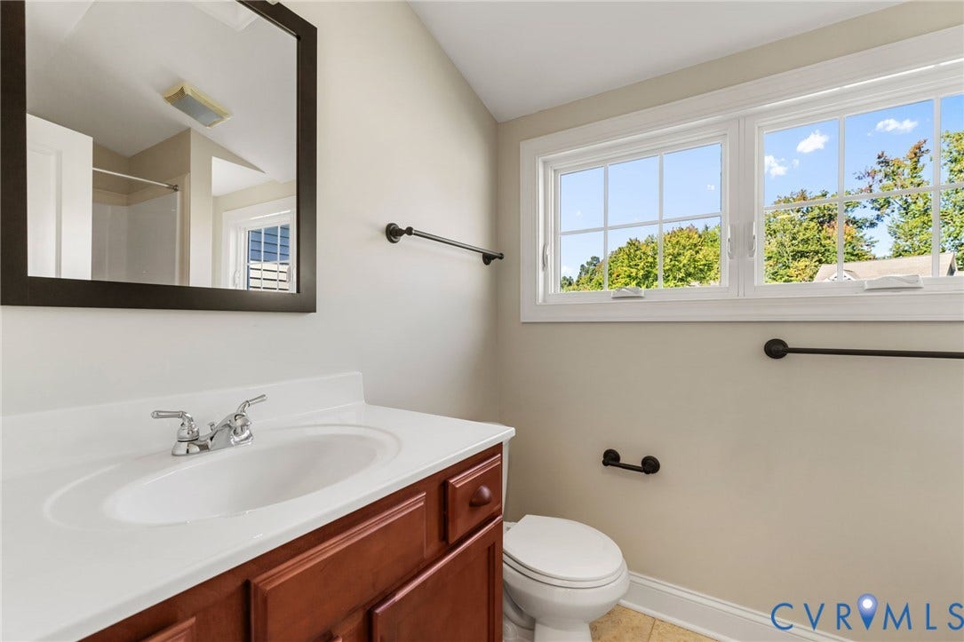 Bathroom featuring a wood-finish vanity with an integrated sink, polished chrome faucet, a large framed mirror, and dual windows