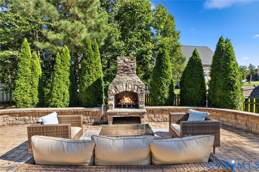 Paver patio featuring a stone fireplace, stone retaining walls, and mature evergreen trees
