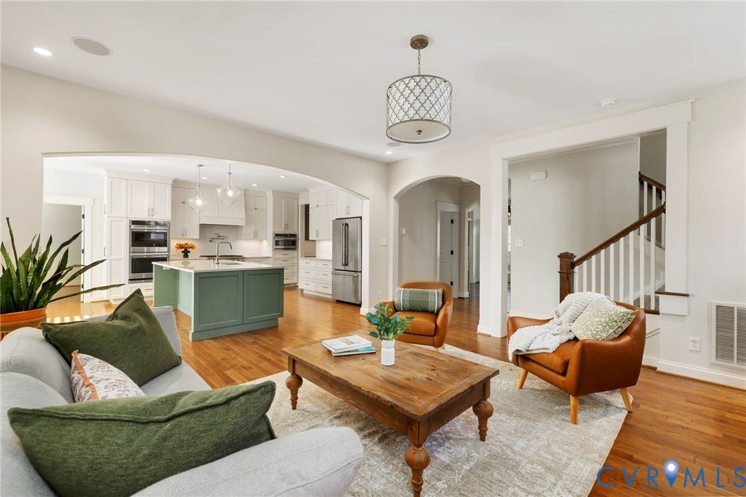 Hardwood flooring throughout, arched doorways, white cabinetry, a green kitchen island with a light-colored countertop, and a contemporary chandelier