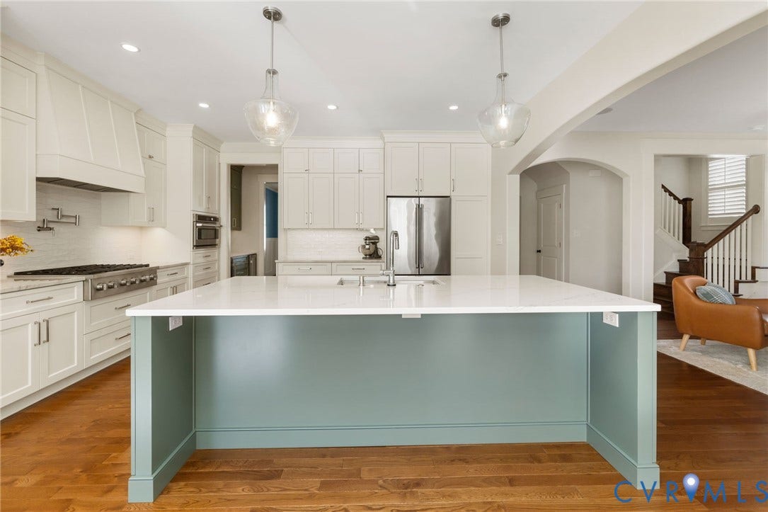 Kitchen featuring a large island with a light-colored countertop, stainless steel appliances, extensive white cabinetry, and wood-finish flooring