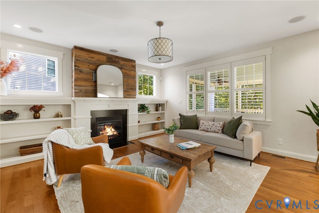 Hardwood flooring, built-in shelving, wood-clad fireplace surround, fireplace with black insert, and white plantation shutters