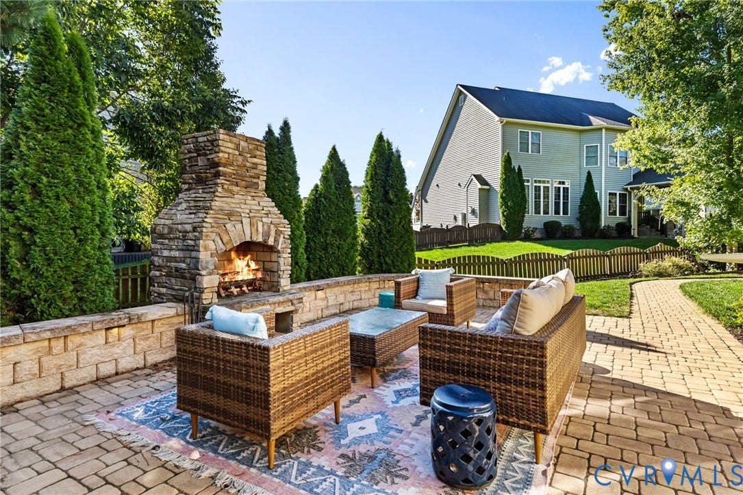 Expansive paver patio featuring a stone outdoor fireplace, stone retaining wall, and a paver pathway