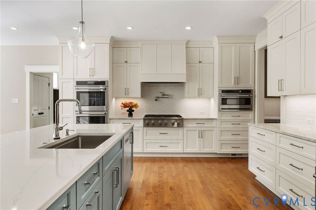 Stainless steel appliances, white shaker-style cabinetry, wood-finish flooring, light-colored countertops, and a kitchen island with an undermount sink