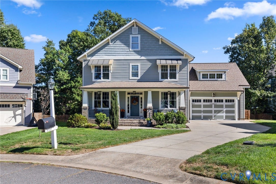 Two-story residence featuring light gray siding, front porch with stone accents, attached two-car garage, and a concrete driveway