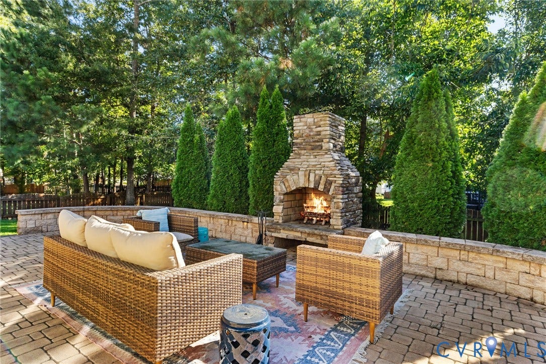 Paver patio featuring a stone fireplace, stone retaining wall, and mature landscaping
