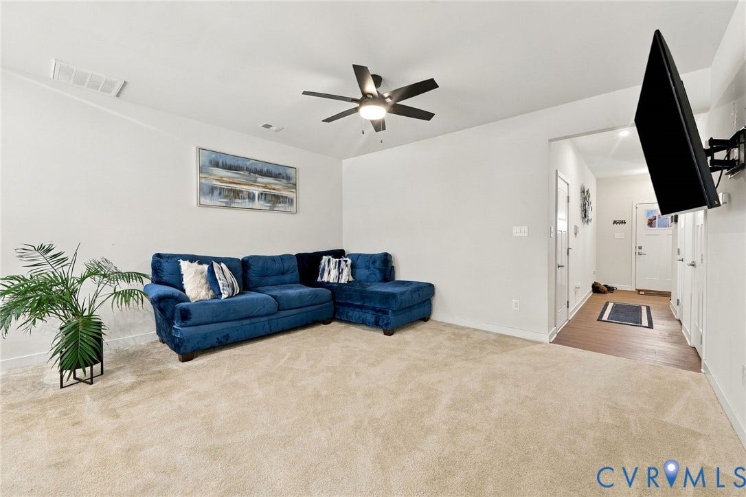 Vaulted ceiling with a ceiling fan, carpeted flooring, and a wood-finish flooring entryway