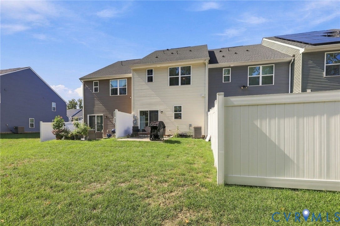 Expansive grassy yard with a private patio area, privacy fencing, and multiple rear windows