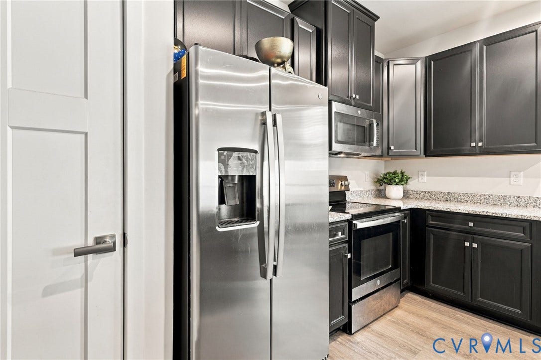 Stainless steel refrigerator, black cabinetry, granite-finish countertops, stainless steel microwave, and wood-finish flooring