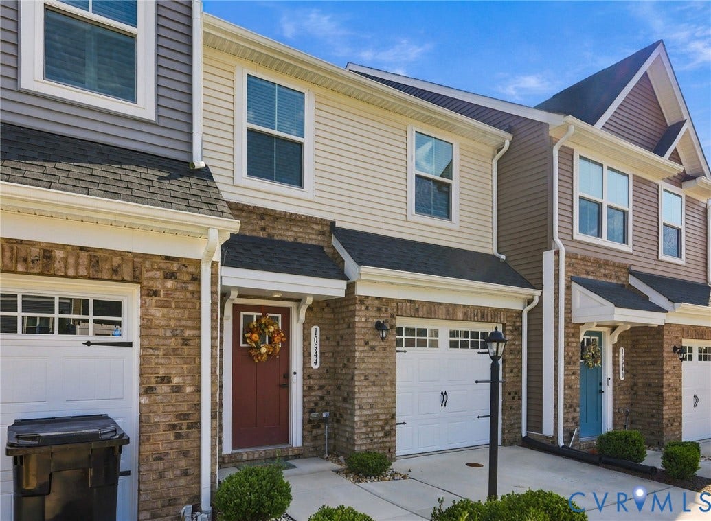 Brick and siding exterior featuring white frame windows, a red entry door, an attached garage, and a paved driveway