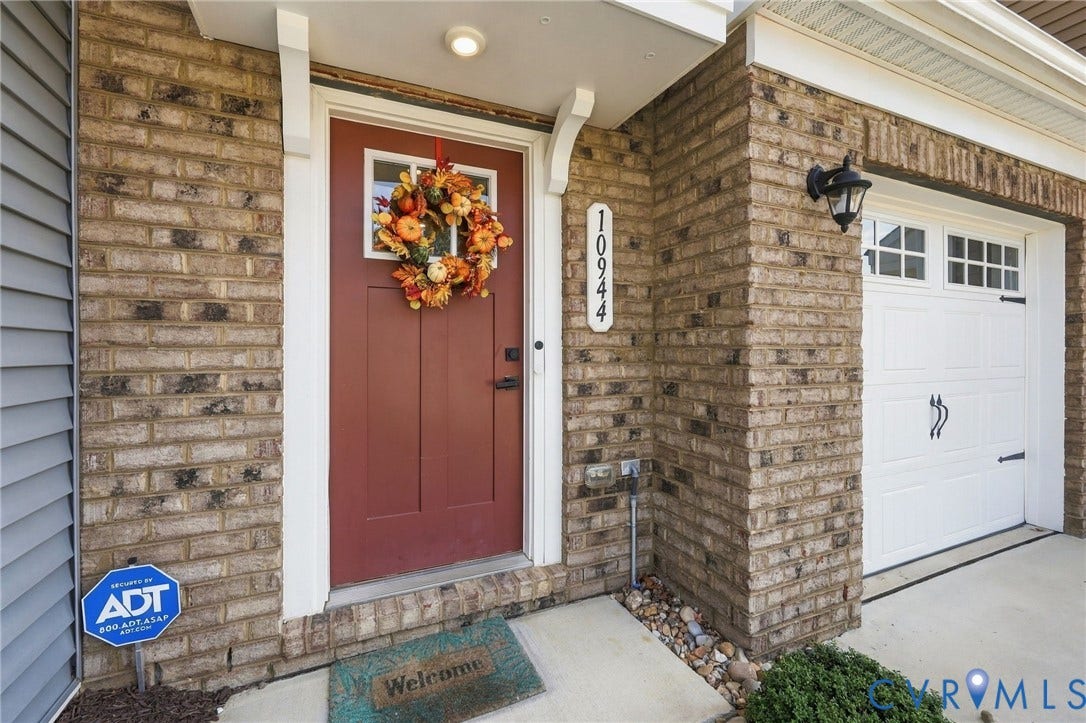Brick and siding exterior featuring a red entry door, decorative address plaque, exterior lighting, and a white garage door with decorative hardware