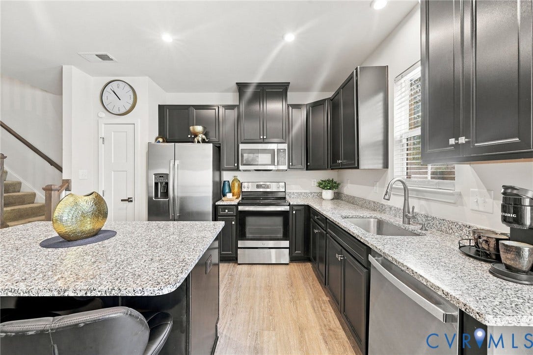 Kitchen featuring dark cabinetry, stainless steel appliances, speckled countertops, and wood-finish flooring