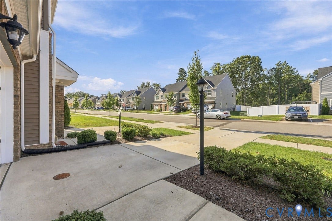Concrete driveway and walkway with landscaping, an exterior wall light fixture, and street lighting