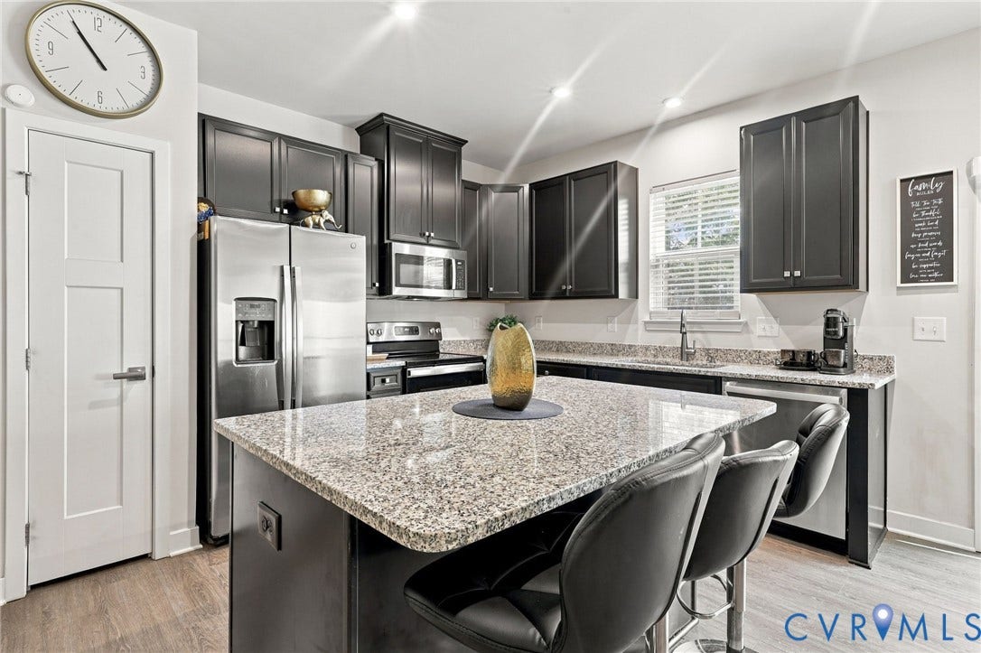 Kitchen featuring dark wood-finish cabinetry, stainless steel appliances, speckled stone countertops, and a central island with counter seating