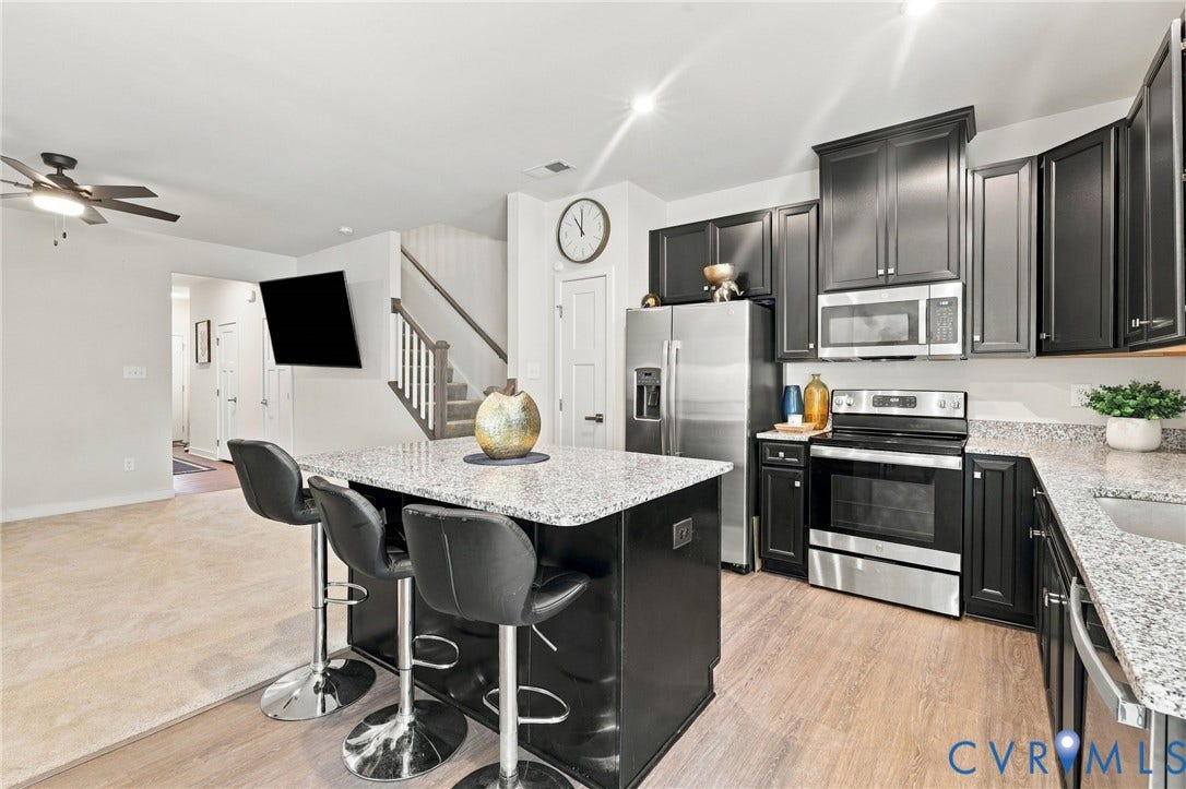 Kitchen featuring dark cabinetry, stainless steel appliances, a center island with a light-toned countertop, and wood-finish flooring