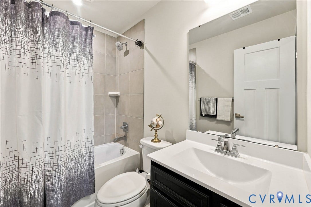 Tub-shower combination with tiled surround, single-sink vanity with white countertop, and framed mirror