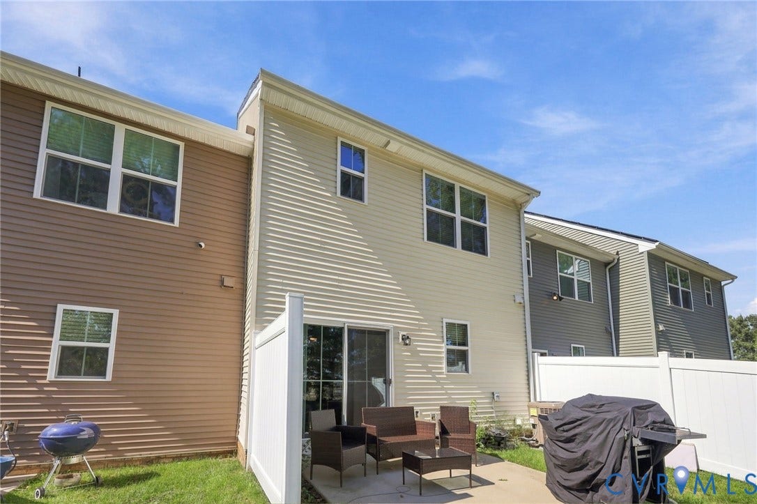 Paved patio area, white vinyl privacy fence, sliding glass door, and multiple windows with white frames