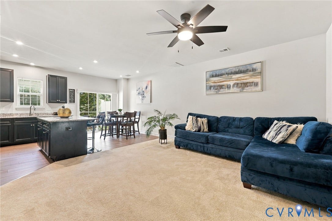 Open-concept living space featuring a ceiling fan, recessed lighting, wood-finish flooring, a kitchen island with seating, and dark cabinetry