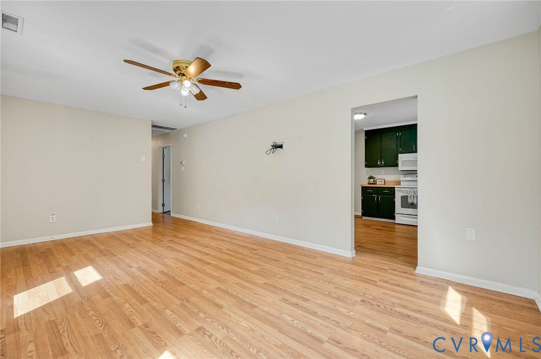 3530 Glisson Road, Richmond, VA 23237 Hardwood-style flooring throughout, ceiling fan with light fixture, and a doorway leading to the kitchen featuring dark cabinetry and white appliances