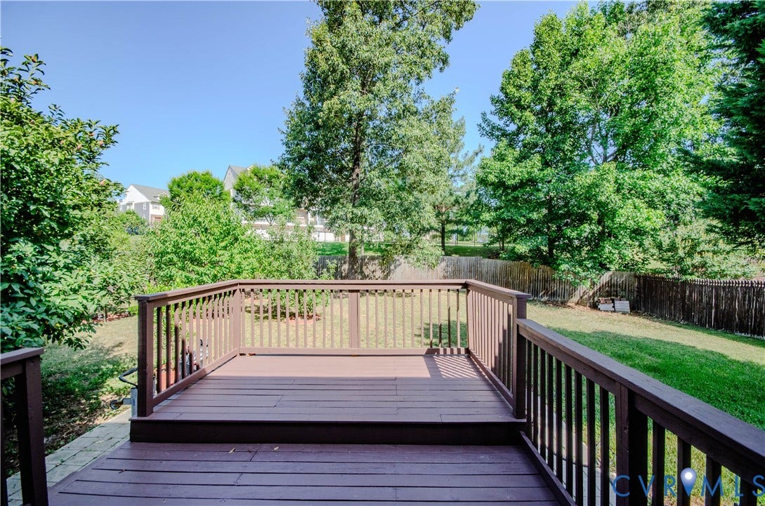 Raised wood deck with wood railing, overlooking a fenced yard with mature trees and a residential backdrop