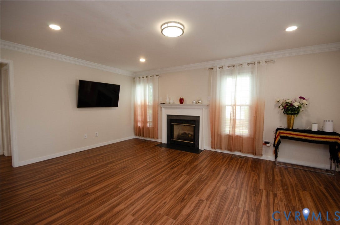 Wood-finish flooring, recessed lighting, crown molding, fireplace with white mantel, and ceiling-mounted light fixture