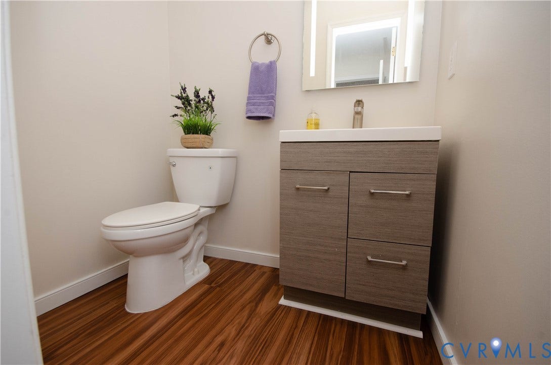 Wood-finish flooring with a white toilet, a modern vanity, and an illuminated mirrored cabinet