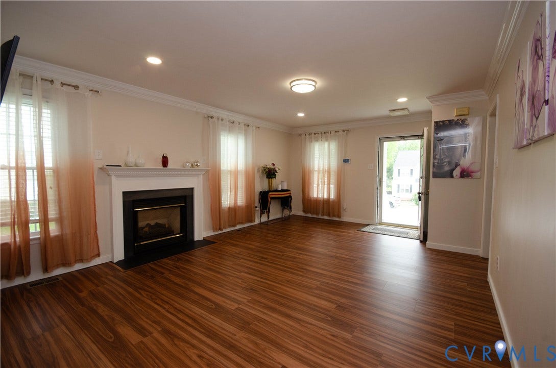 Spacious room featuring wood-finish flooring, a fireplace with a white mantel, recessed lighting, and crown molding