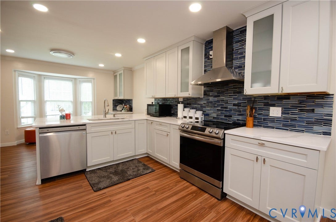 White cabinetry with glass-front accents, stainless steel appliances, wood-finish flooring, a mosaic tile backsplash, and recessed lighting