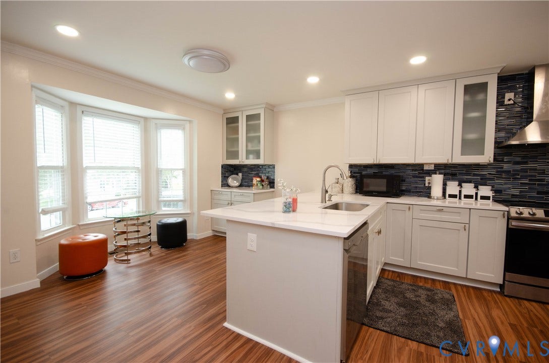 Bay window with blinds, wood-finish flooring, recessed lighting, white cabinetry, and stainless steel appliances