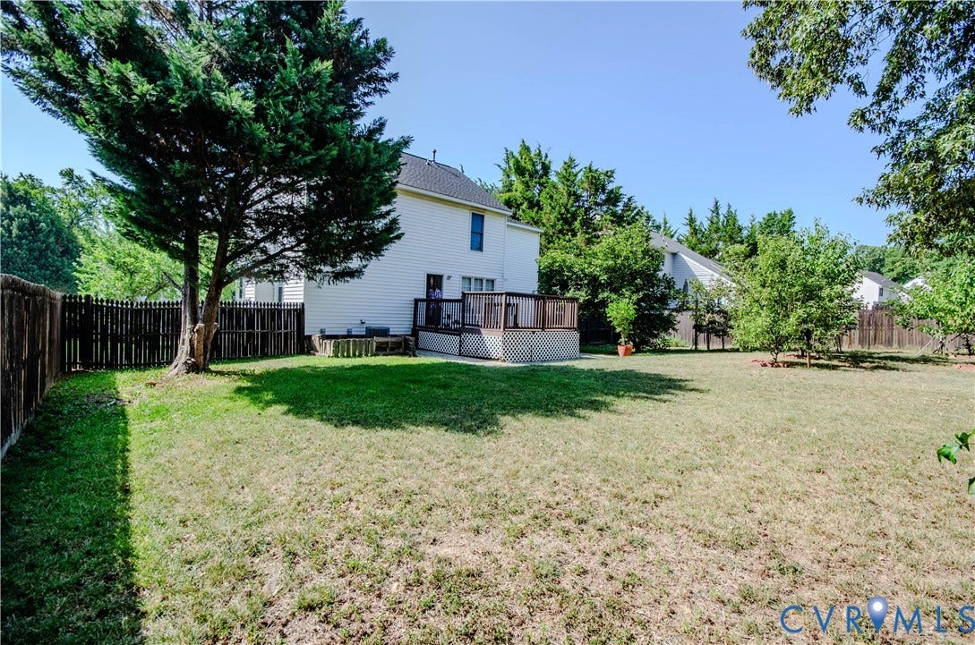 Expansive backyard featuring a large wood deck with lattice skirting, mature trees, and privacy fencing